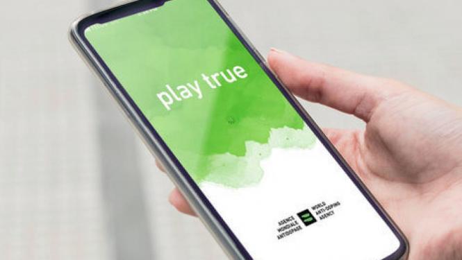 Cilvēka plauksta, kas rokās tur viedtālruni, kura ekrānā ir attēlots attēls ar tekstu "Play True"